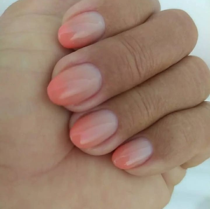 Mão com unhas naturais decoradas com esmaltação em degradê, variando do tom rosado ao transparente.